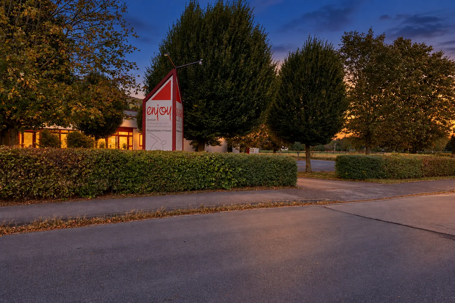 Die Einfahrt zum enjoy im Westhof Meschede mit dem Schild am Straßenrand, in der Abenddämmerung